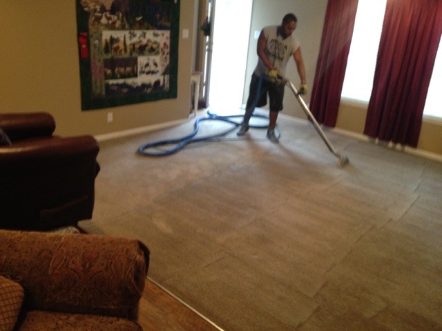 Nichol's technician steam-cleaning a living room carpet with a truck-mounted wand